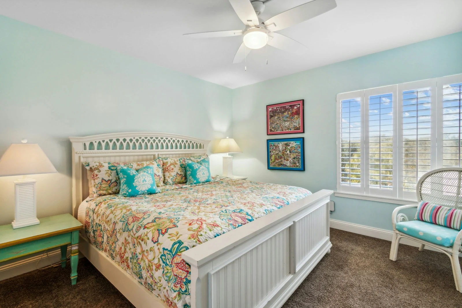 Coastal bedroom with aqua accents, a white bed, and bright shuttered windows